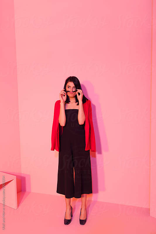 fashion model wearing black outfit and red jacket posing under colored lights