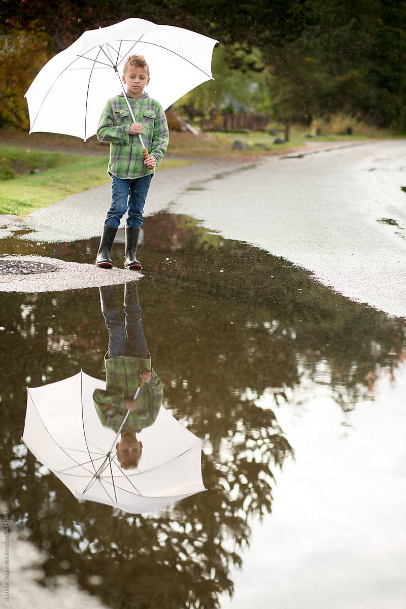 somber Boy with umbrella plays in puddle