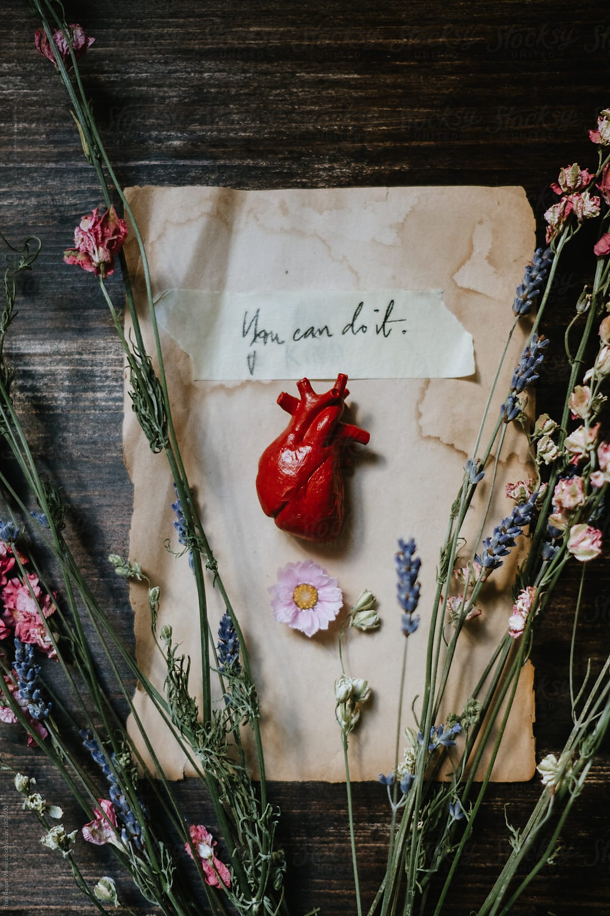 little human heart over a written piece of paper surrounded by flowers