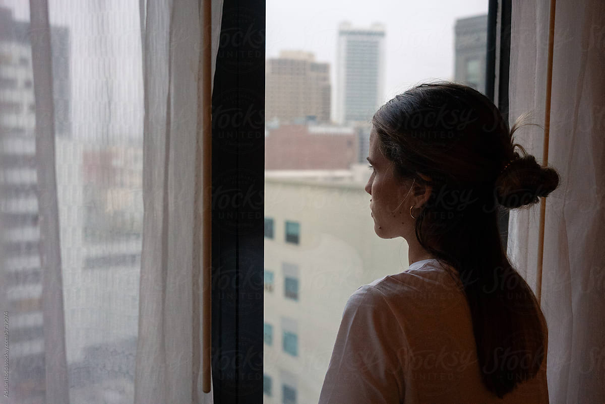 A woman watches the streets from the window of his apartment