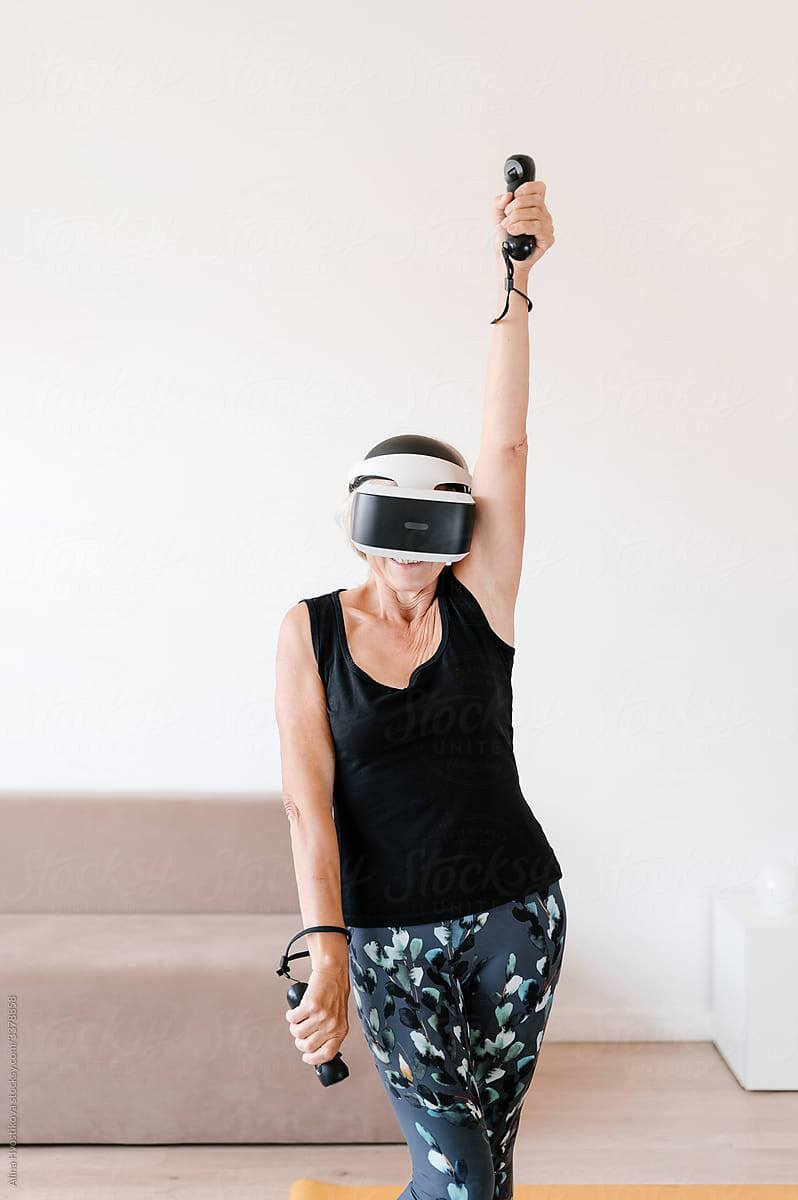 Senior sportswoman in VR headset exercising at home