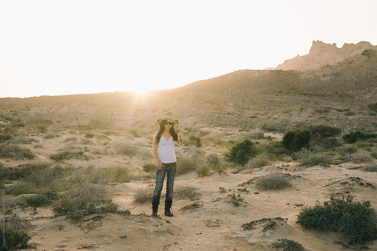 sexy woman in cowgirl look standing in the desert at sunset