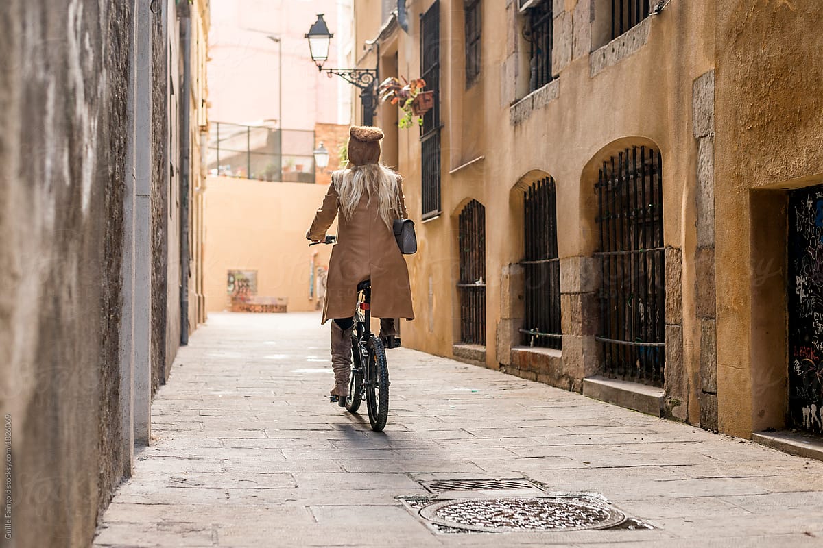 Woman cycling on bike along narrow street.