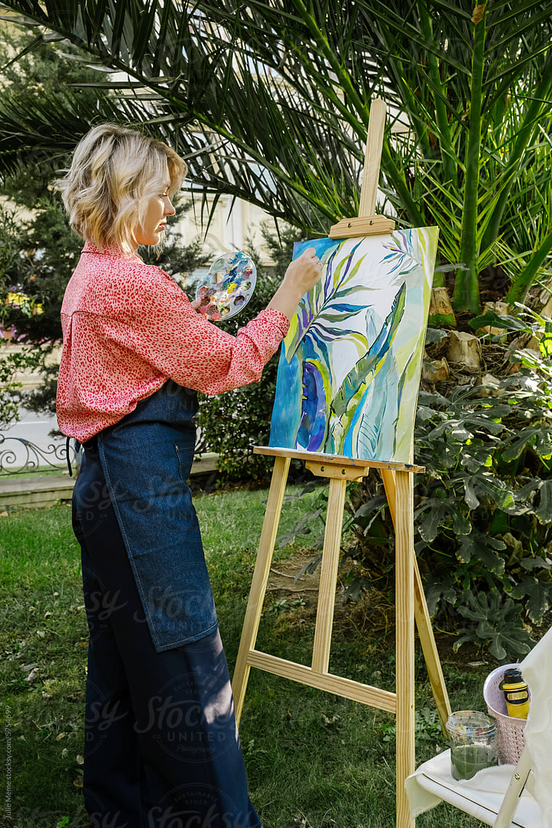 The girl with a light bob haircut stands sideways and paints outdoors