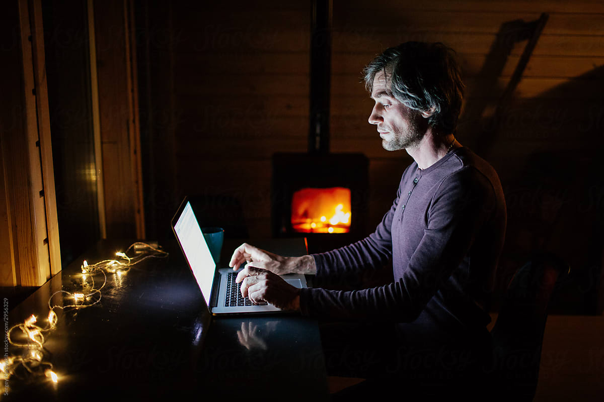 Freelancer working on laptop at night near fireplace