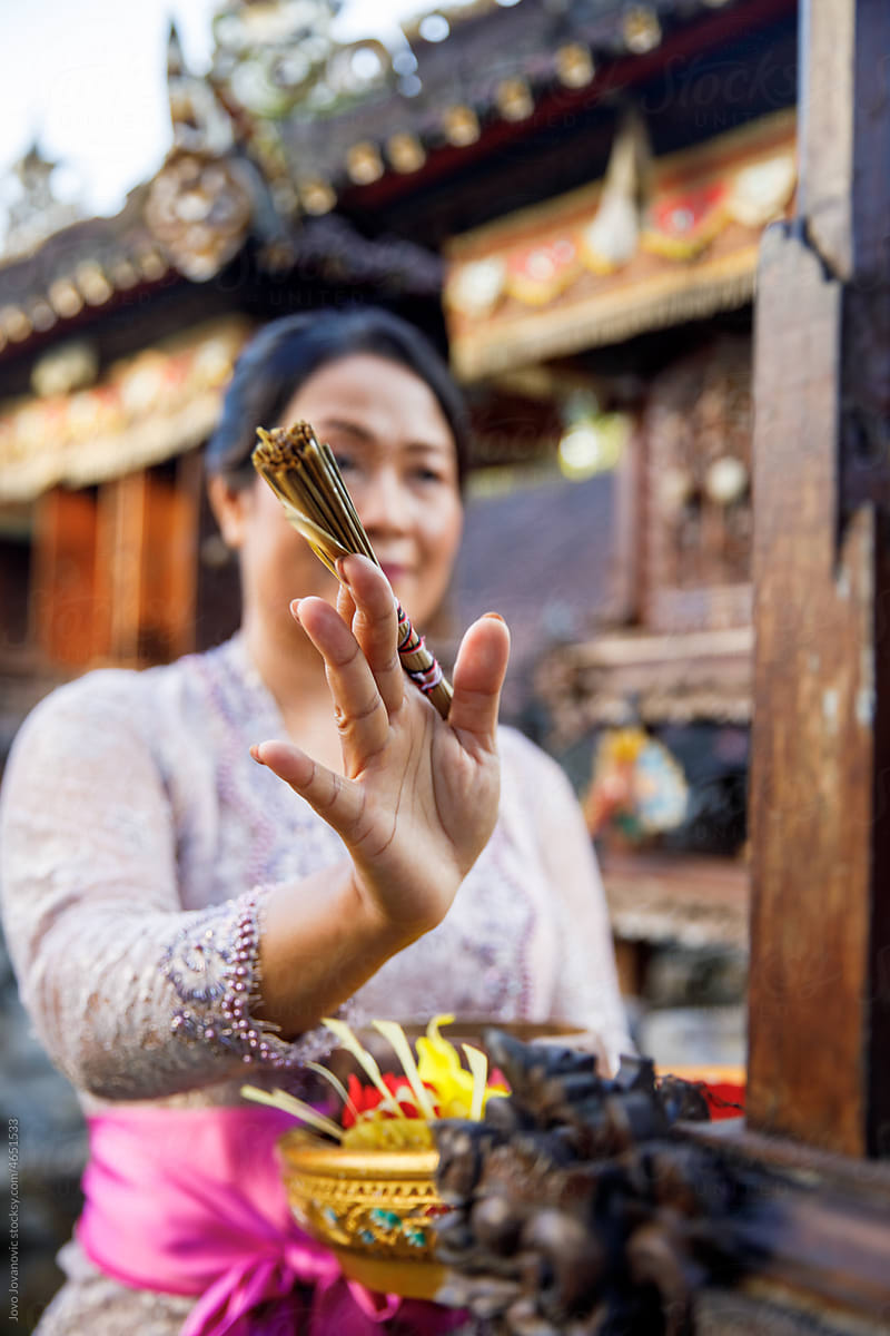 Balinese woman praying in front of a Hindu temple with incense