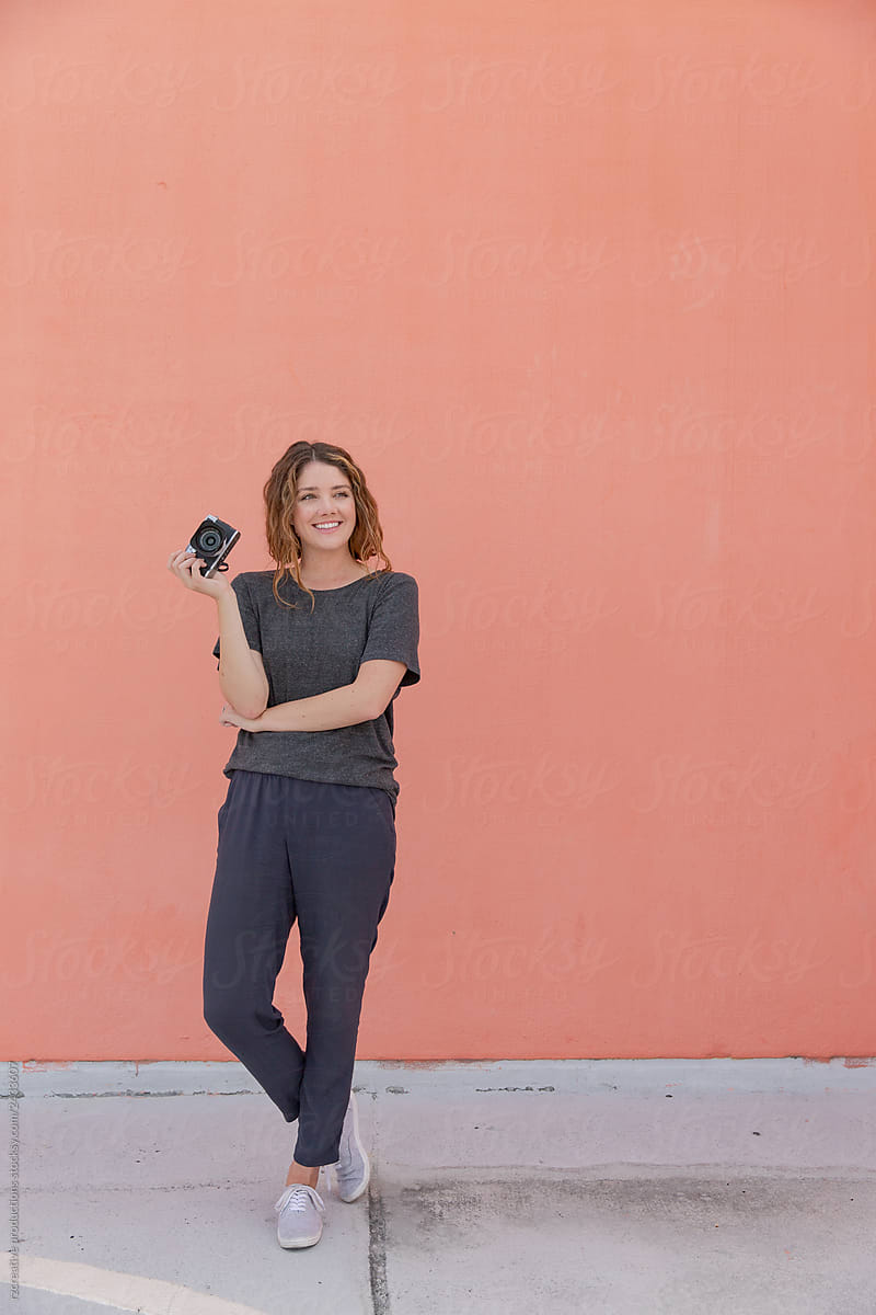 Portrait of woman with camera against blank wall.