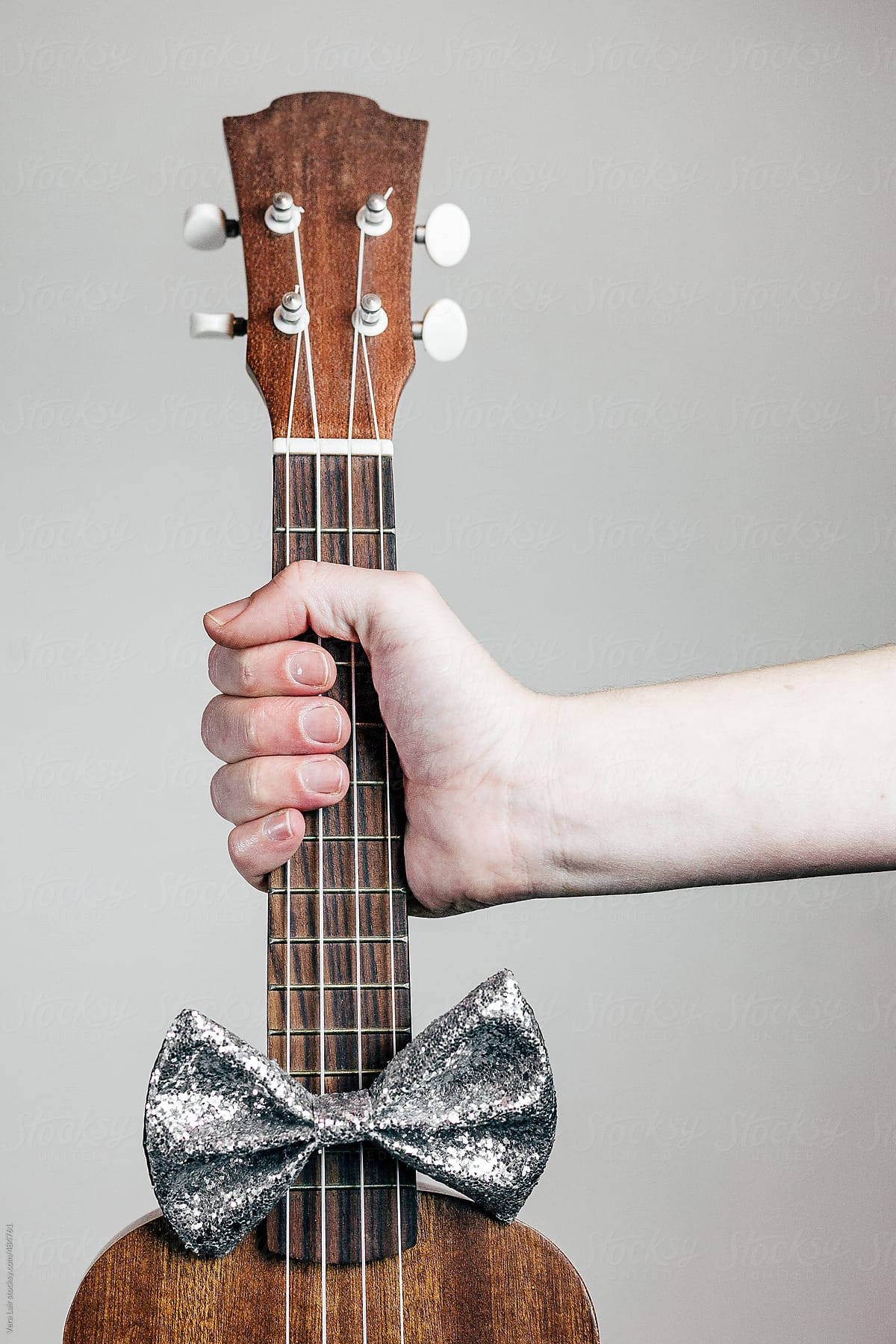 Hand holding a ukulele, with a bow tie
