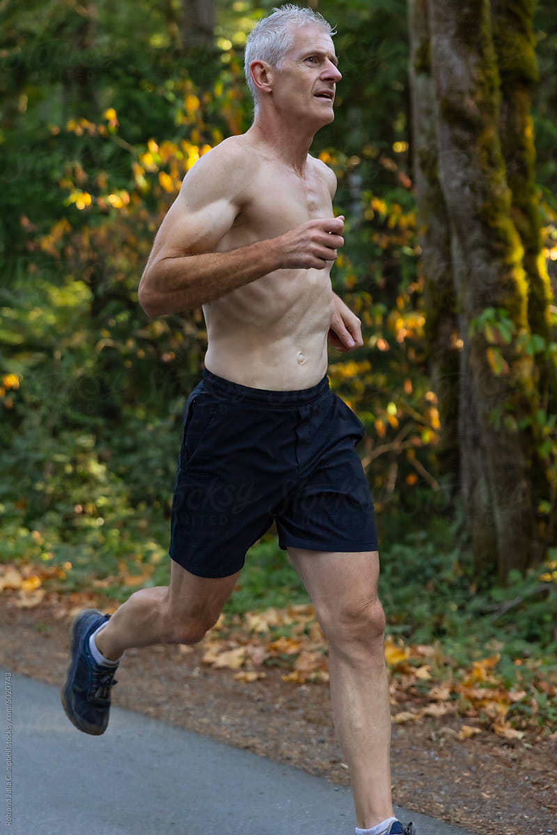 Fit man running hard on road in autumn or fall.