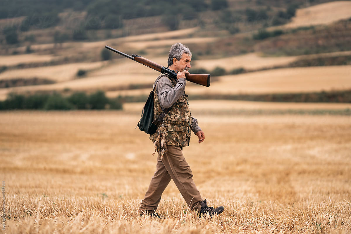 Mature hunter man carrying a shotgun on his shoulder