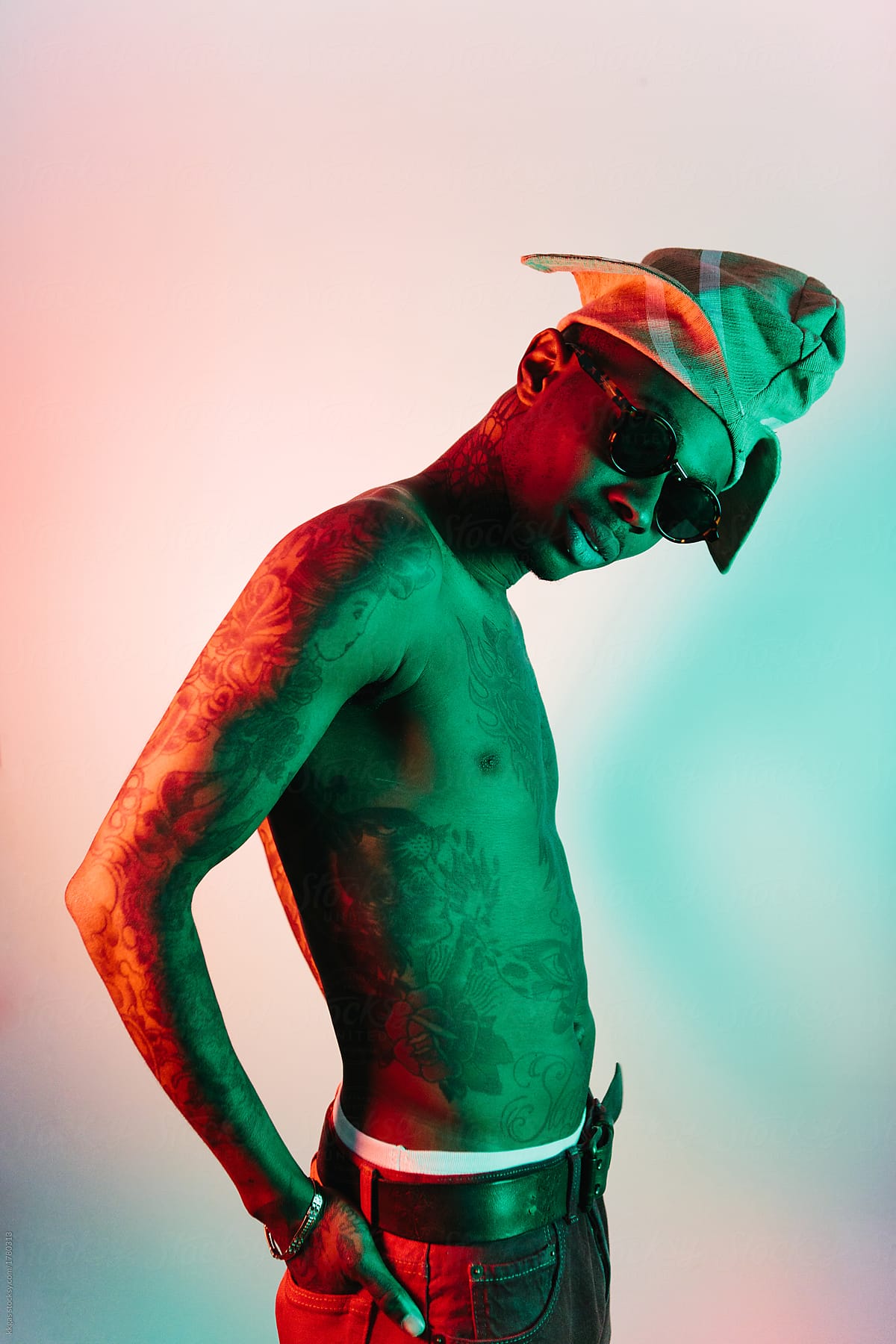 Bare chested heavily tattooed man wearing a Yoruba hat with orange and green lighting