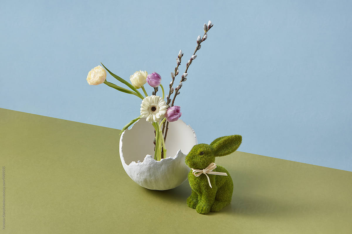 Easter toy next to vase in form of broken eggshell with spring flowers