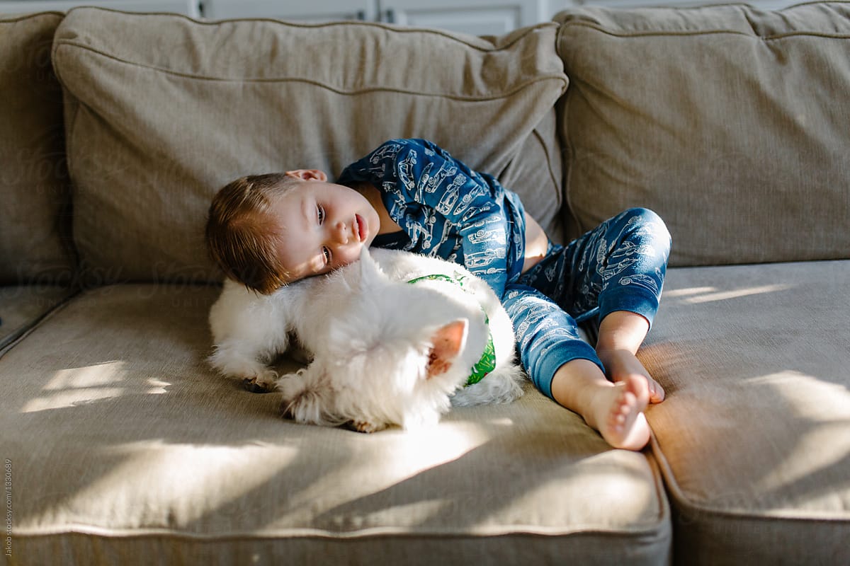 Cute young boy in a pajama snuggling with his dog on a couch