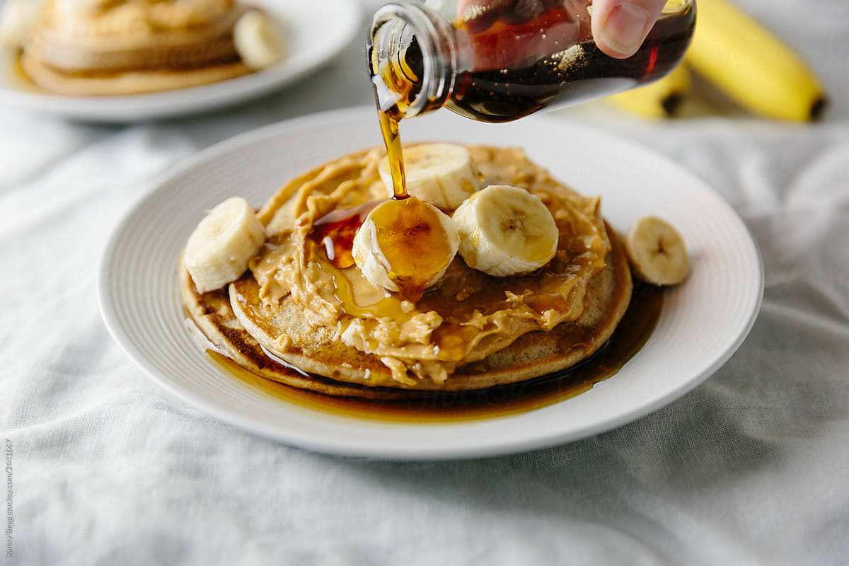 Pouring maple syrup on vegan pancakes with peanut and banana