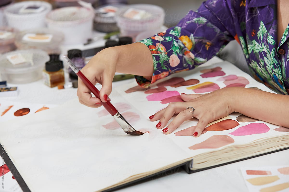 Artist's Hands Using Paintbrush On Book In Art Studio