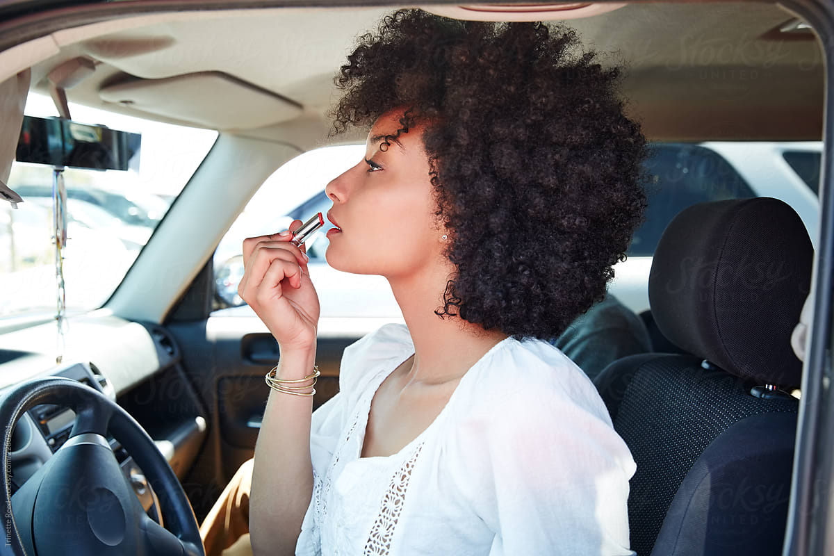 Young ethnic millennial woman putting on lipstick in her car