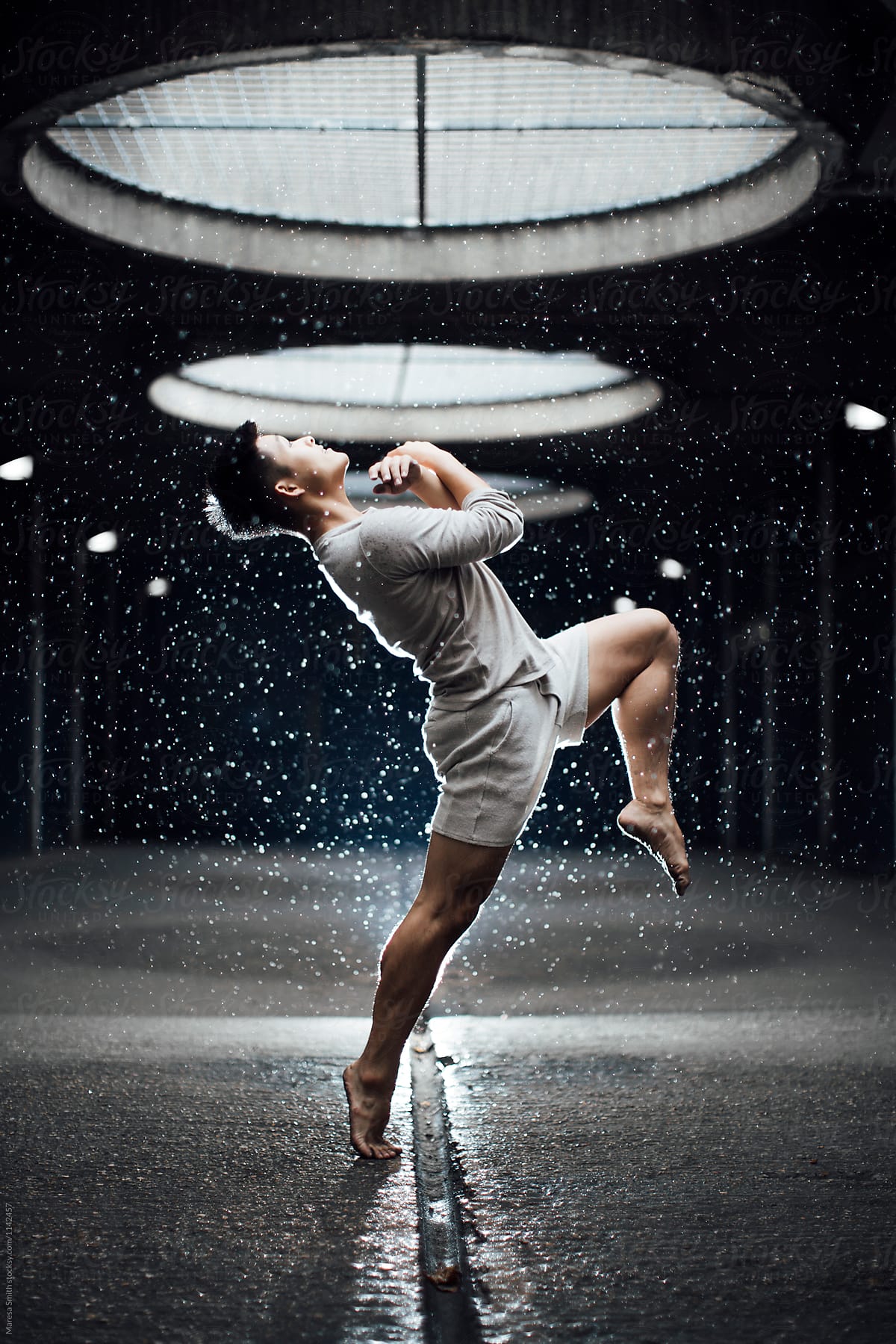 An Asian man dancing in the rain in an unusual urban setting
