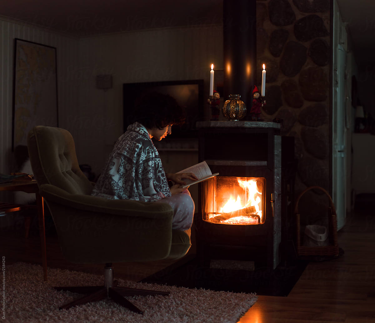 Pretty young woman is reading book near the fireplace.