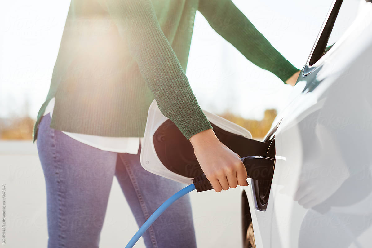 Crop woman recharging electric vehicle