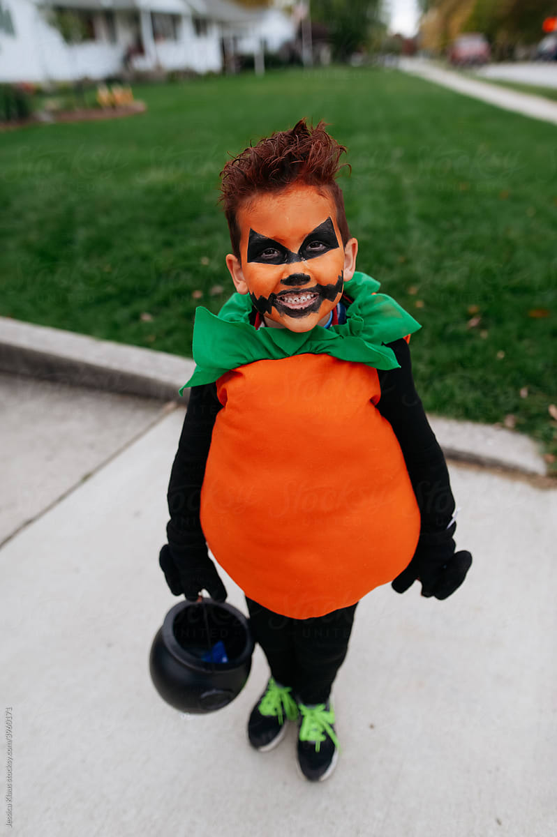 Boy wearing a pumpkin costume standing in the driveway.