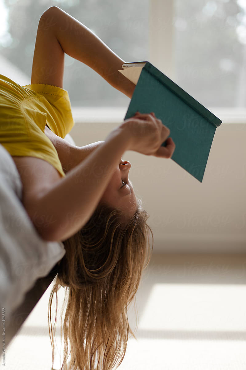 Girl hanging upside down off edge of bed while reading a book