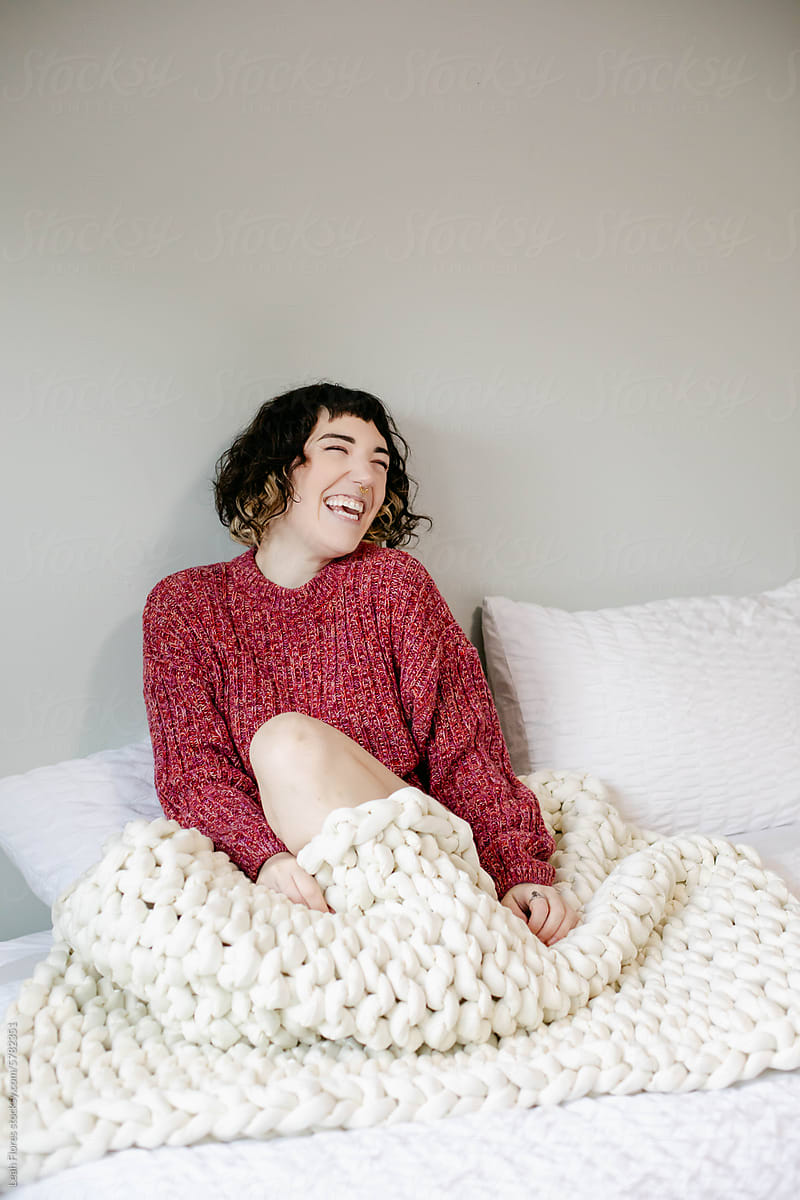Happy, Laughing Woman Cuddled in Bed with Blankets