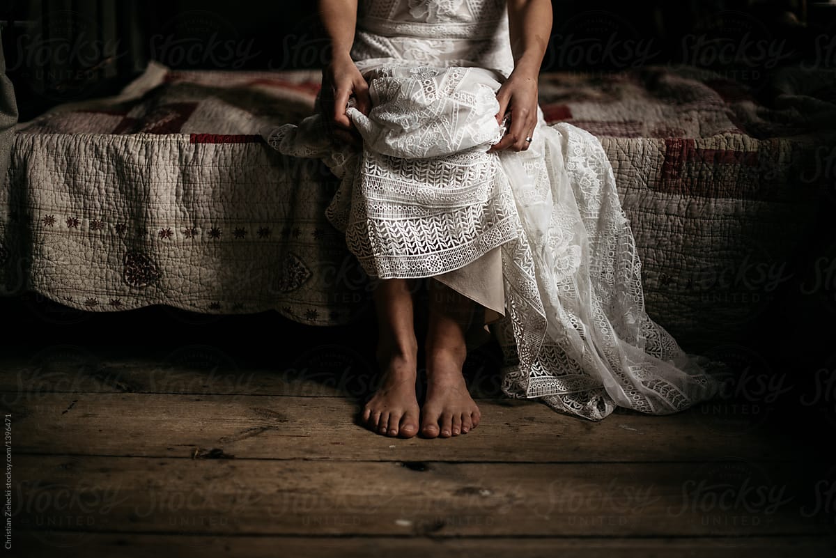 Crop barefoot bride sitting on bed on wedding day
