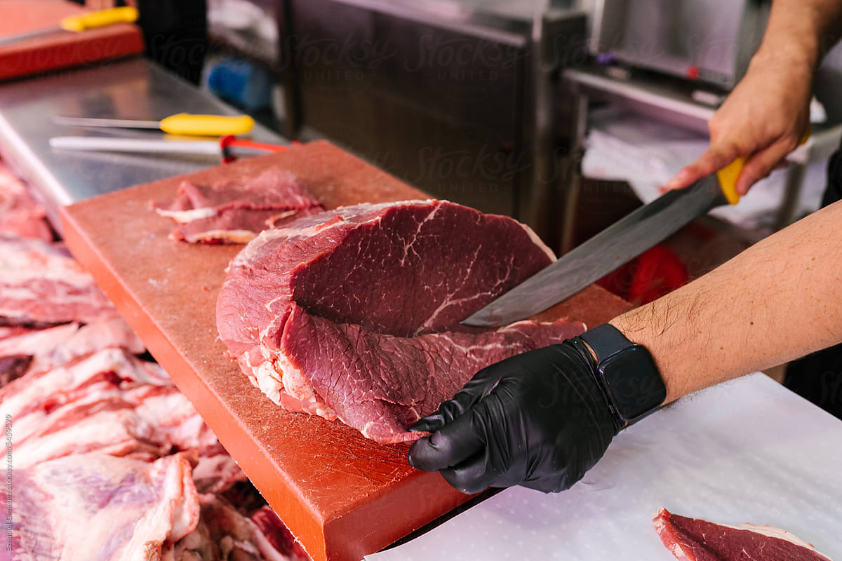 Crop male worker cutting meat on board in kitchen