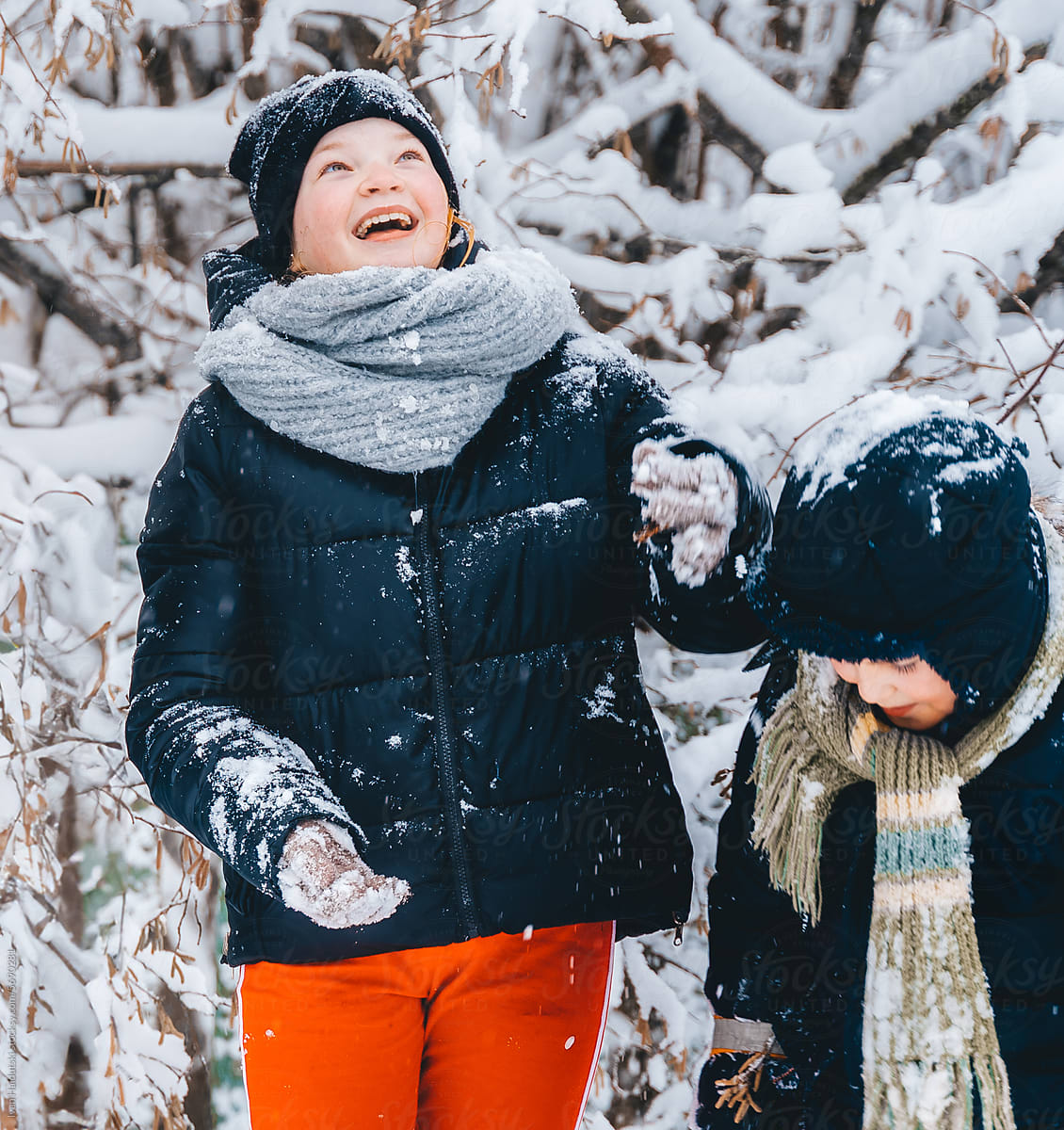 Smiling girl playfully shakes snow on brother\'s head in snowy forest