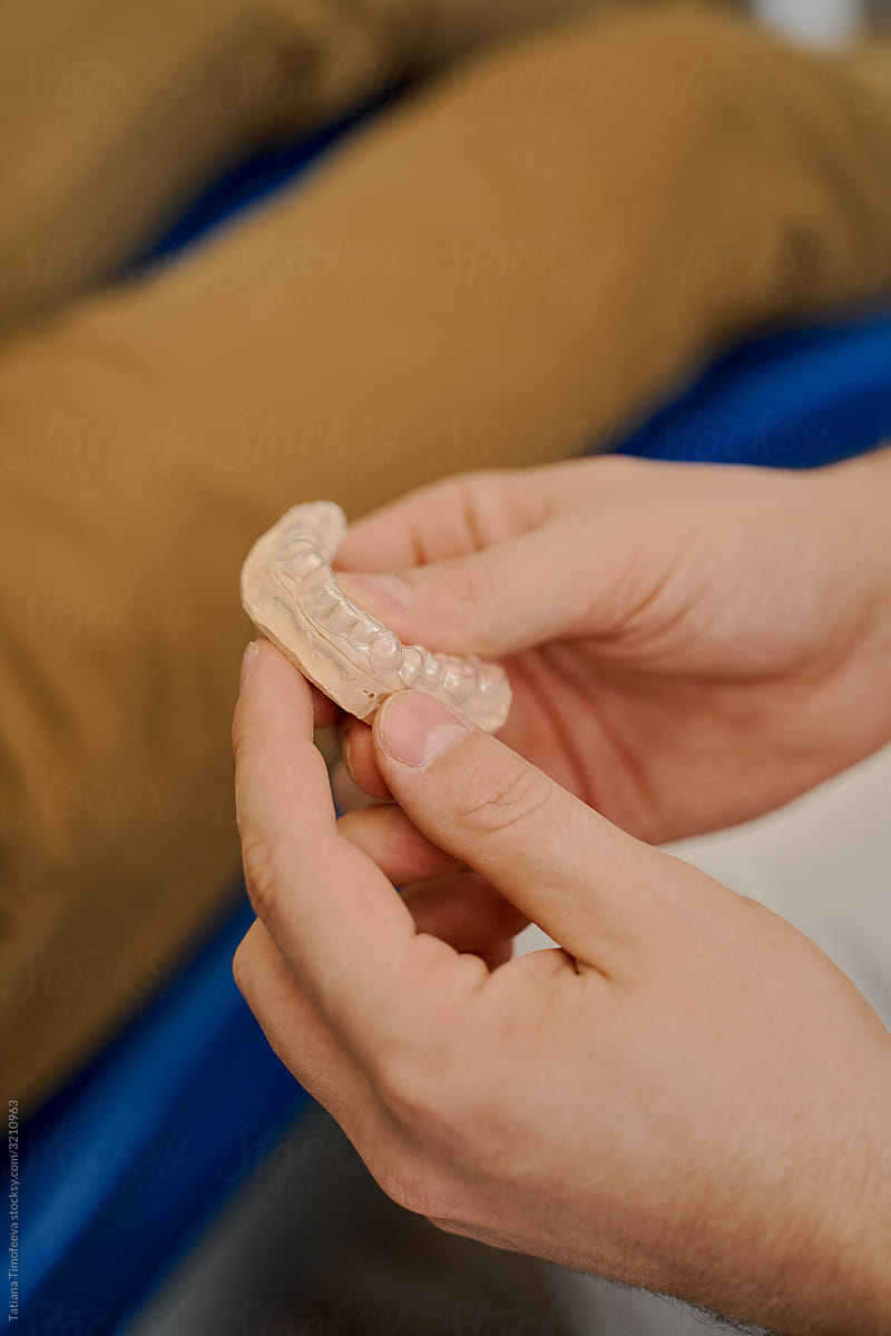 a dentist in a dental clinic holding a cast of teeth from a man's jaw