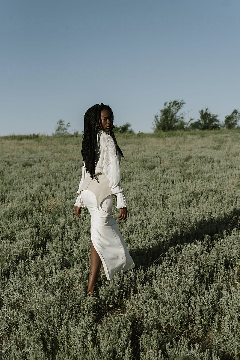 Stylish black woman walking in countryside field in stylish dress