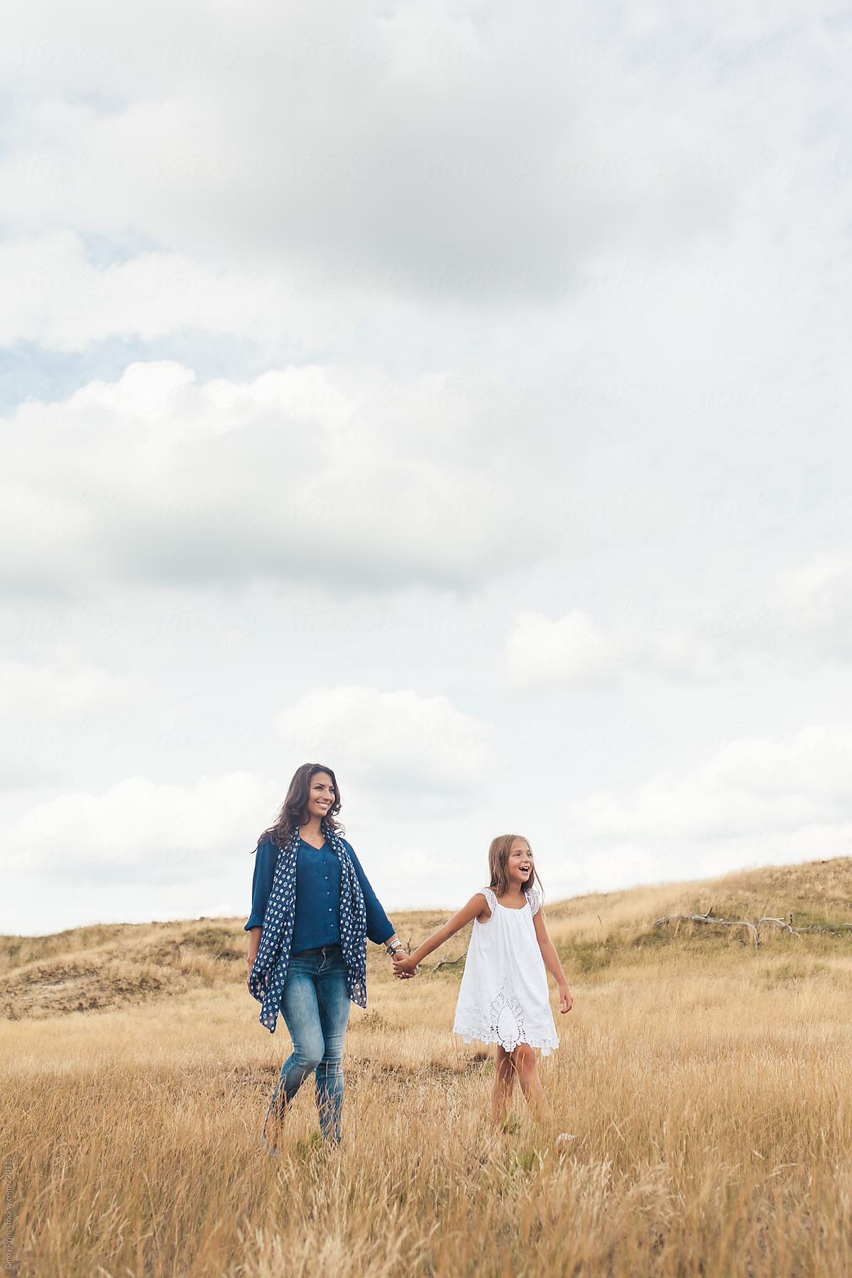Mother and daughter walking in a golden field underneath a big cloudy sky