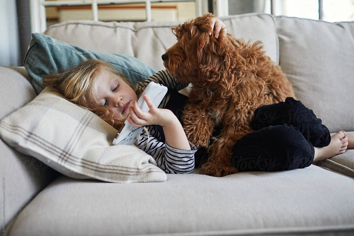 Child playing on a smart phone with her pet puppy dog
