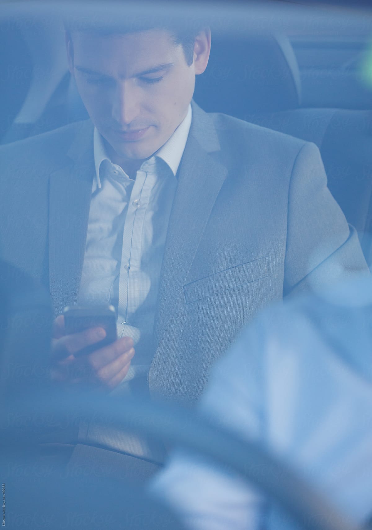 Businessman sitting in a backseat of the car and texting on the phone.
