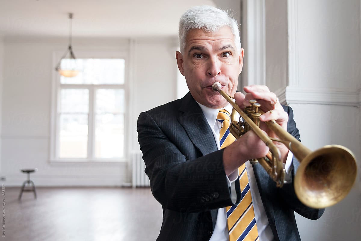 closeup of man in suit blowing into trumpet