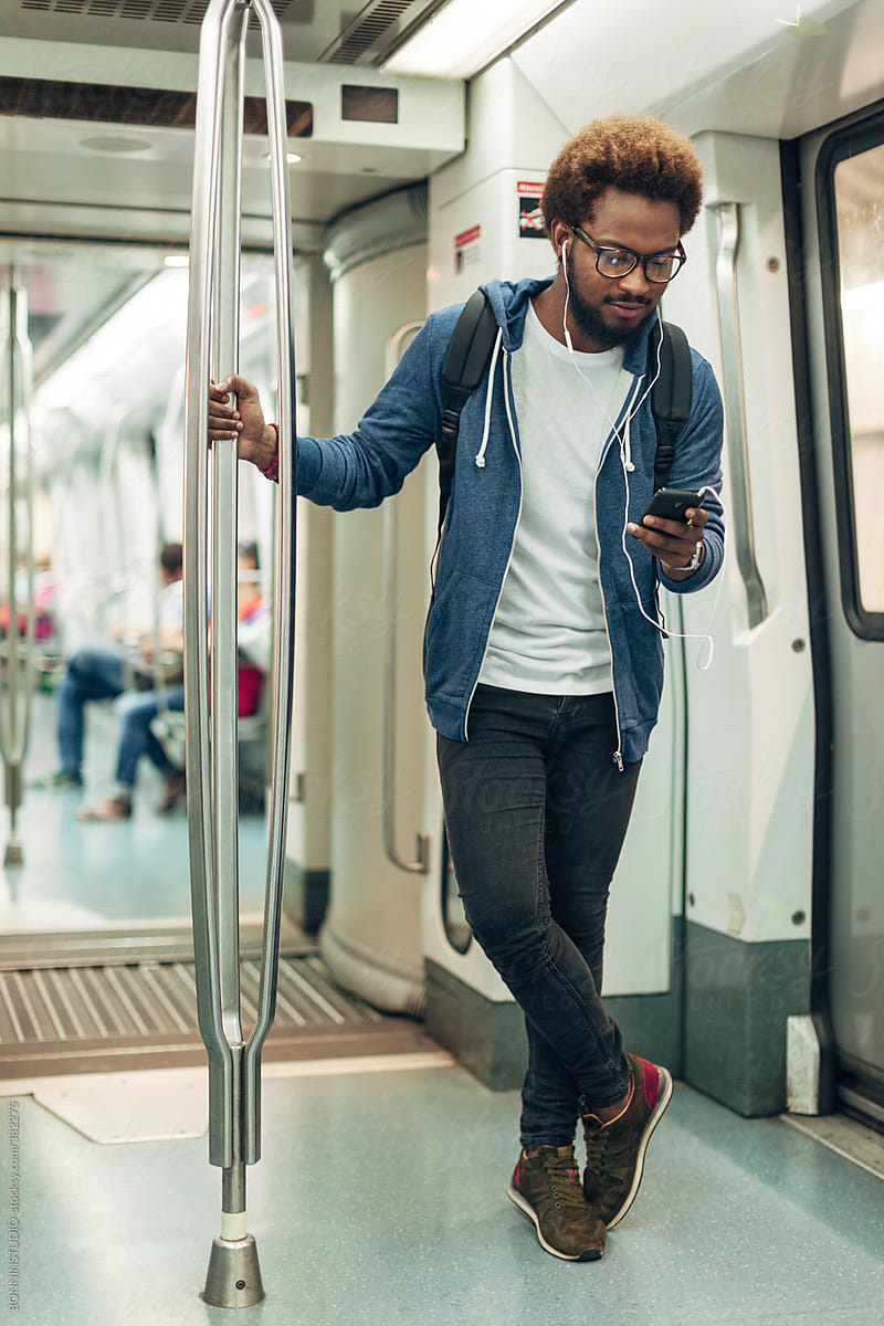 Young afro black man using mobile phone while listening music on the subway train.