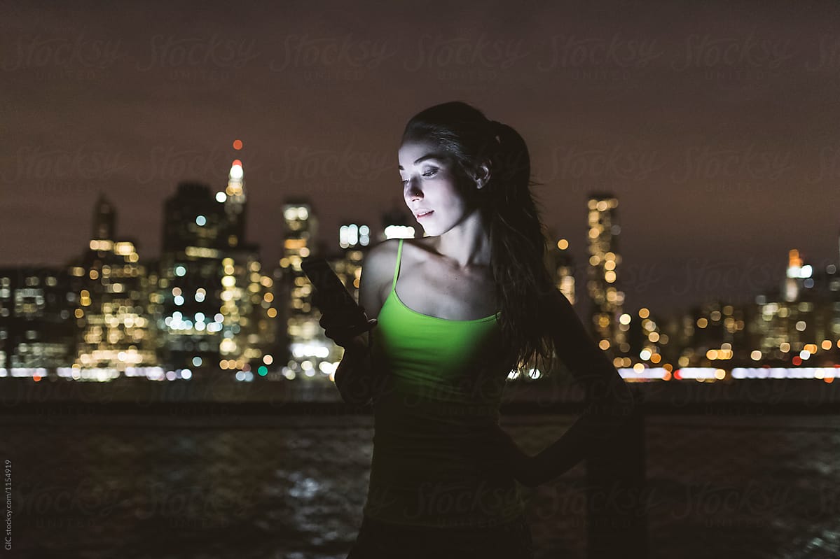 Young woman using technology at night against New York skyline