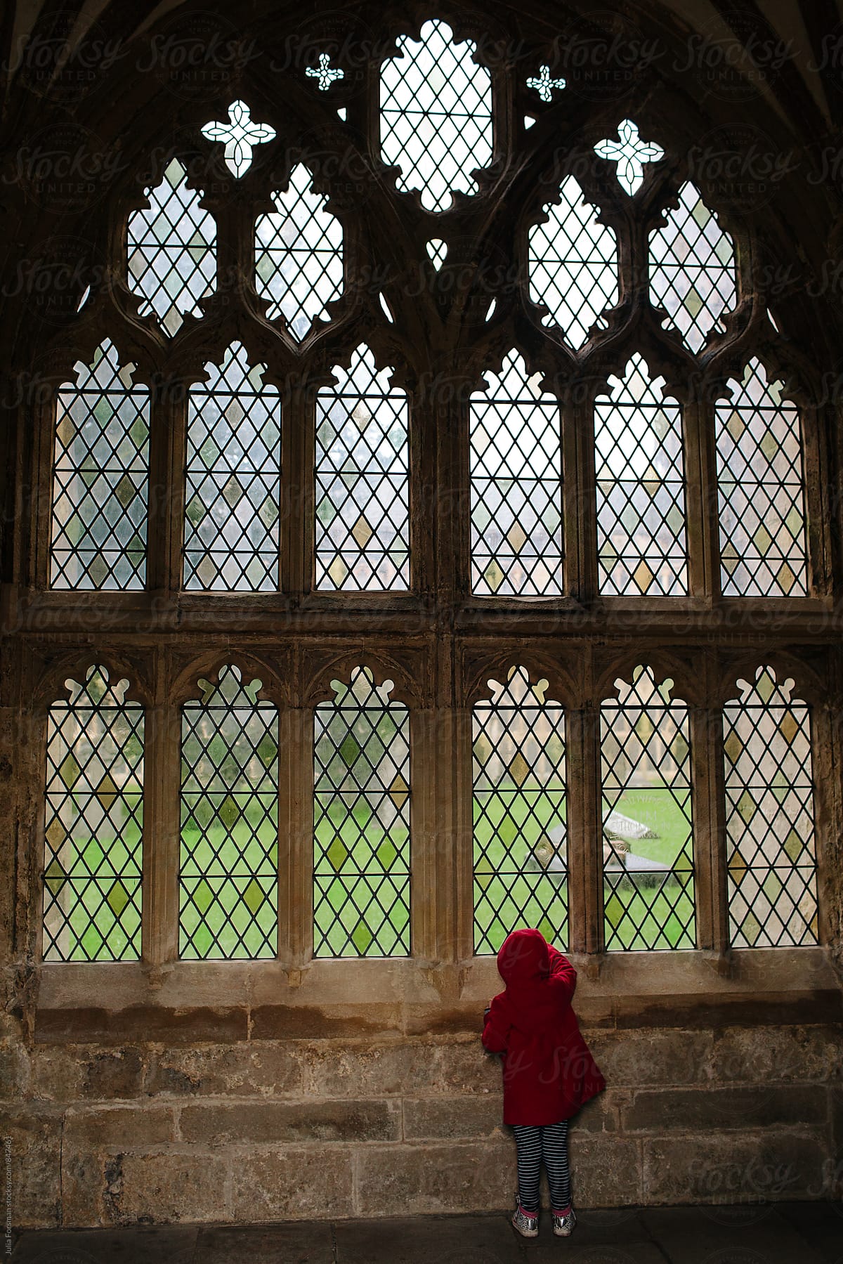 Little girl looking out of a section of a large medieval Gothic window in a cathedral cloister.