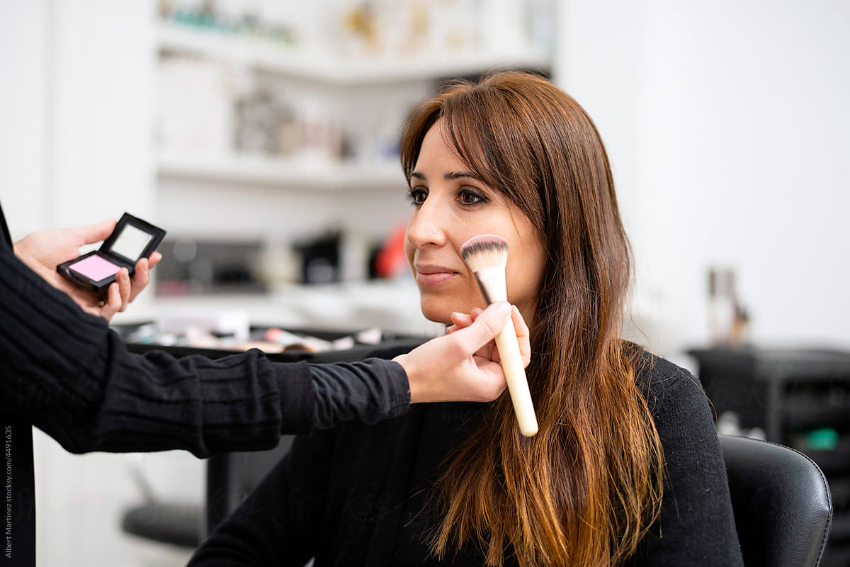 Crop makeup artist applying powder on model face