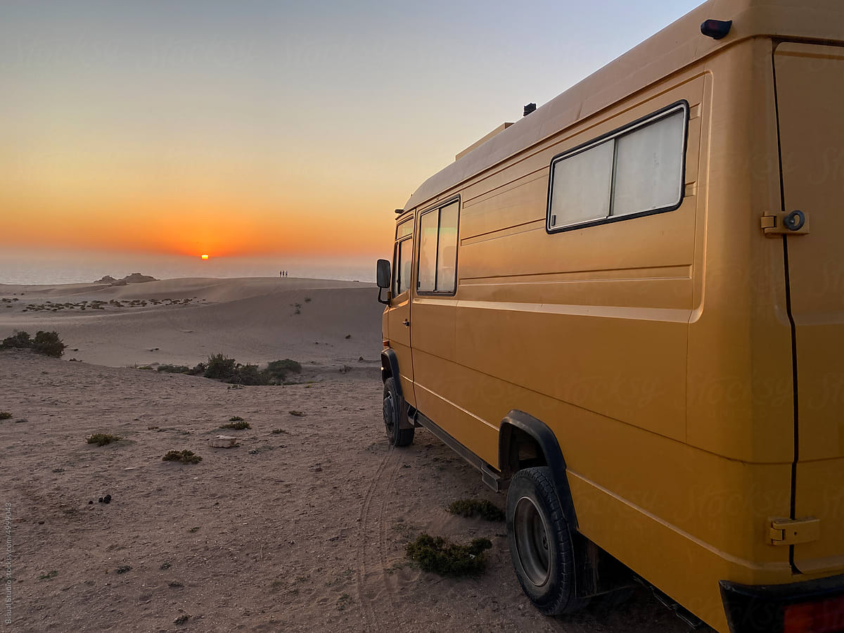 Retro camper parked on sandy dune at sunset