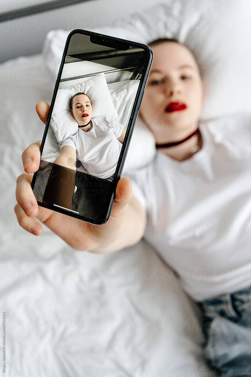 Sensual informal woman taking selfie on smartphone