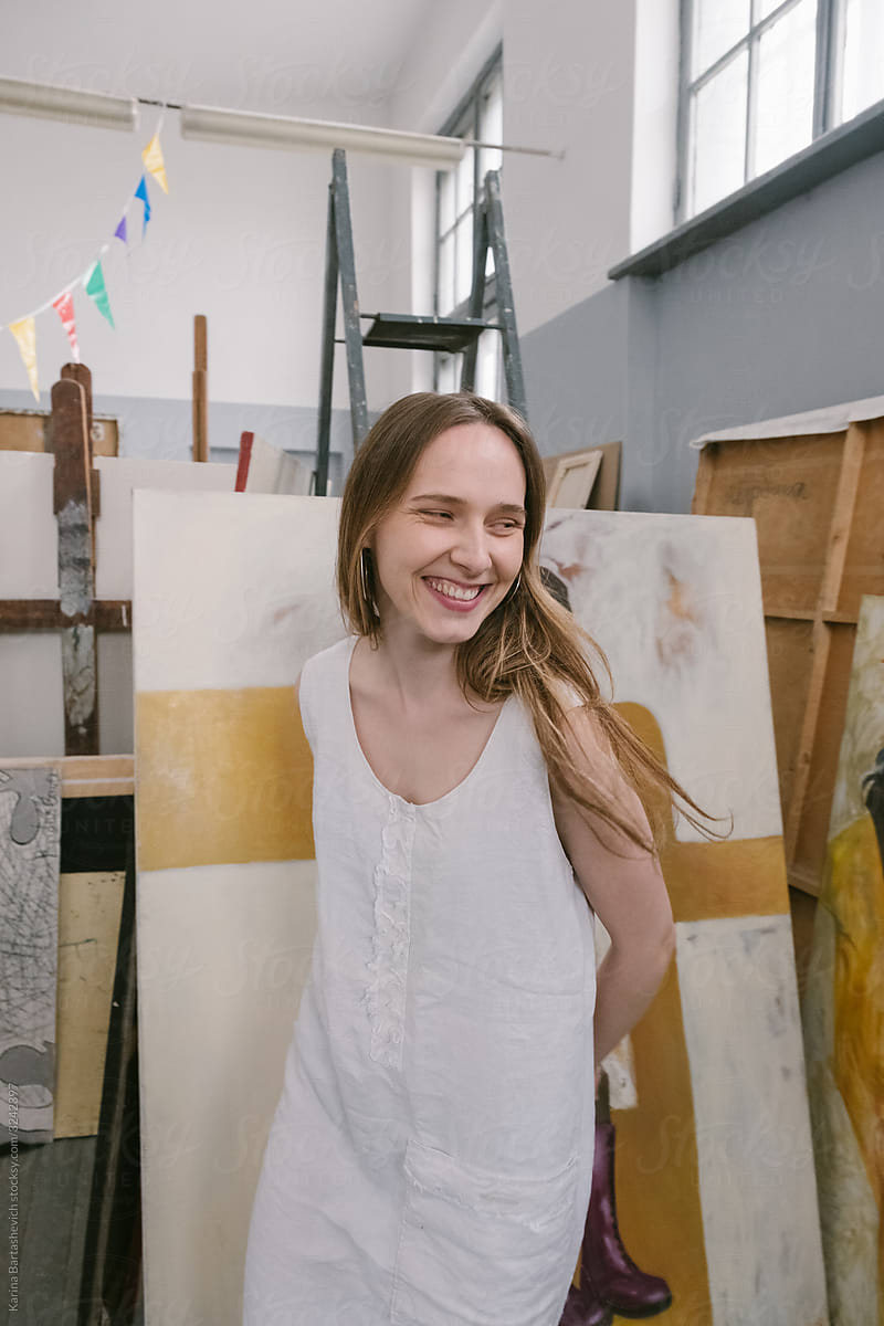 girl artist in the studio next to her paintings laughing looks at the camera