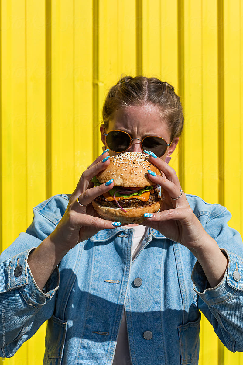 A woman holding a burger in front of her face