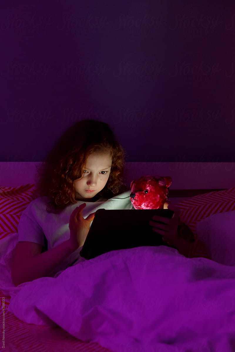 Child with plush toy using tablet before sleep