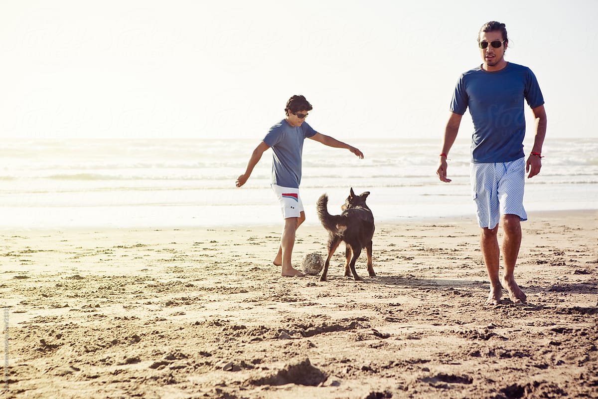 Hispanic-American Men Playing Beach Football with Pet Dog