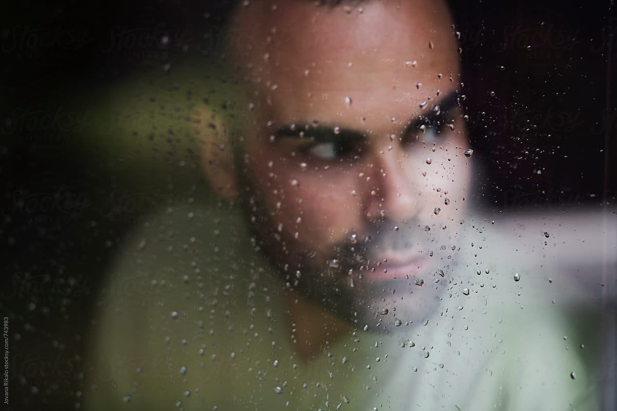 Portrait of a man standing at the window watching the rain