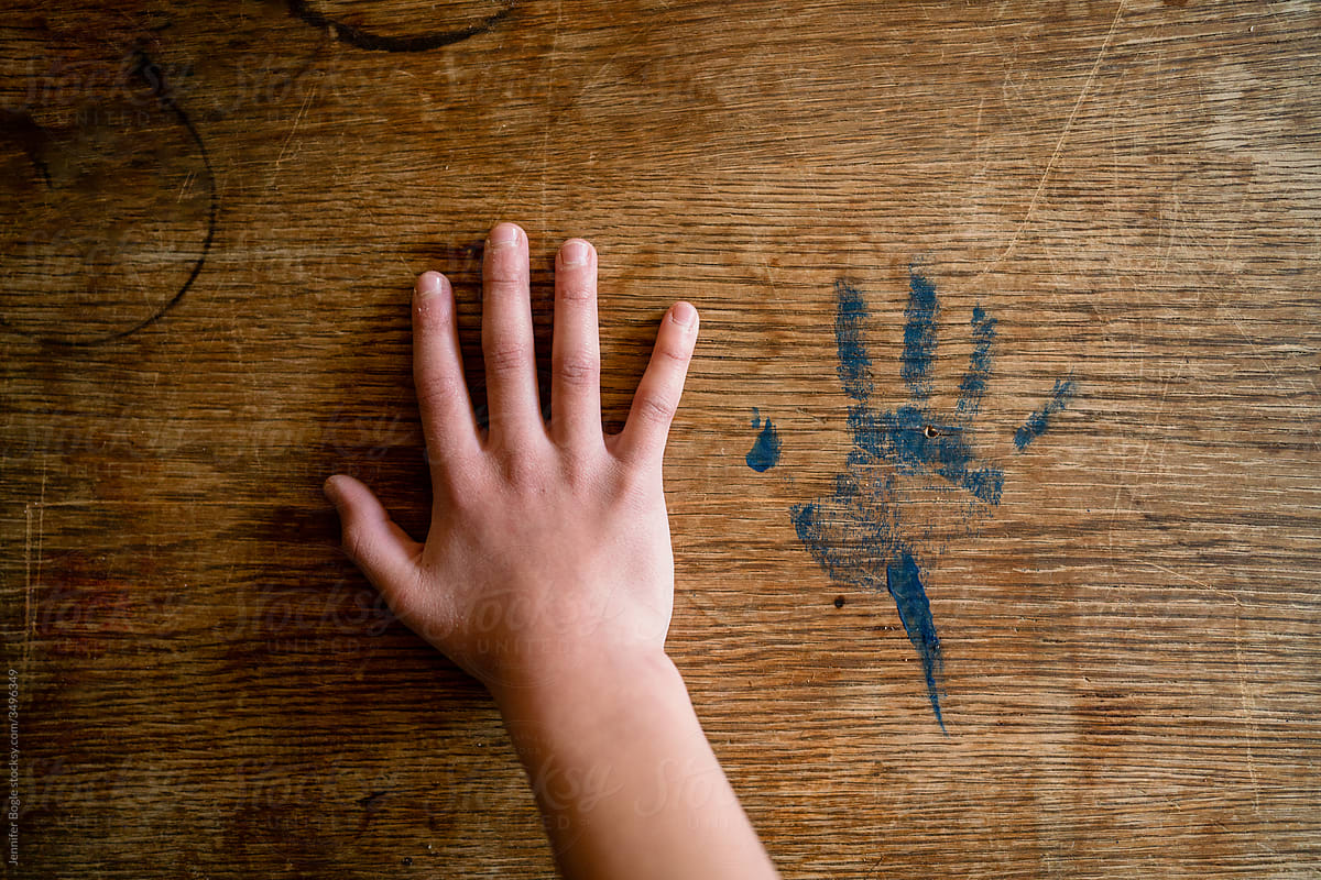 Child holds large hand next to smaller handprint