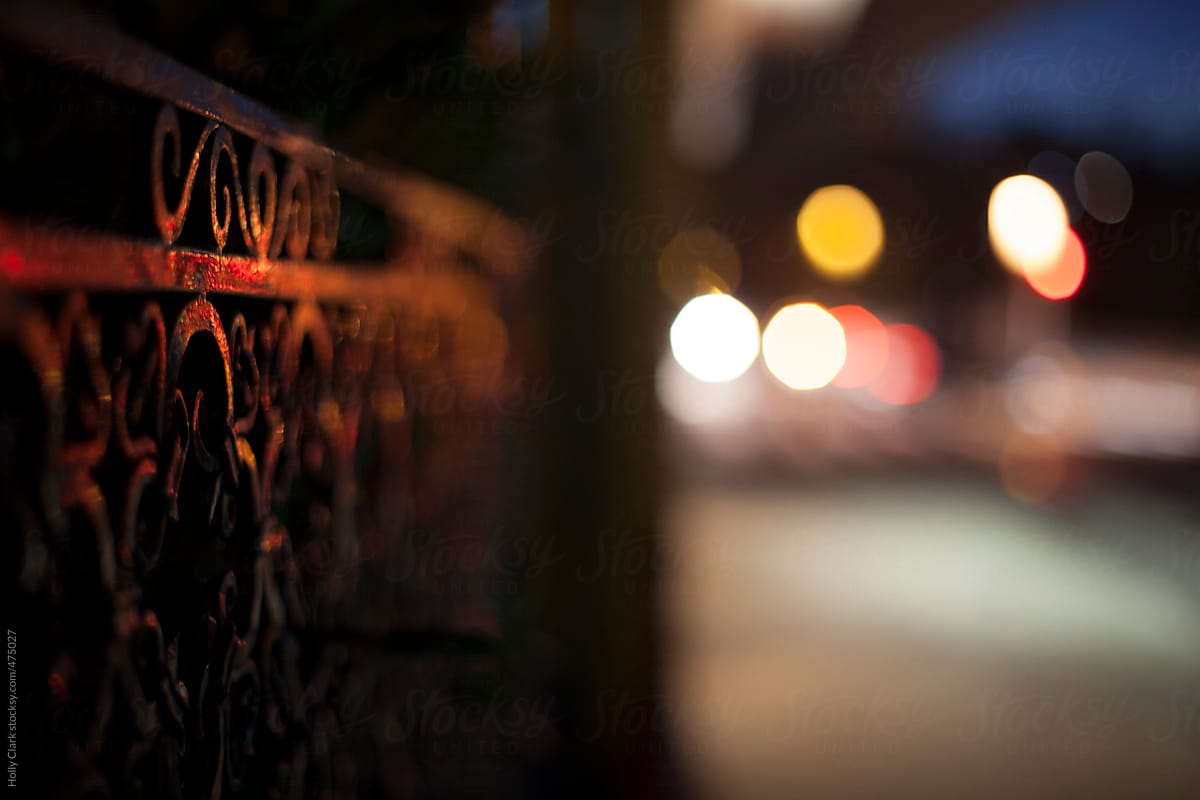 A wrought-iron fence at night with blurred traffic in the background.