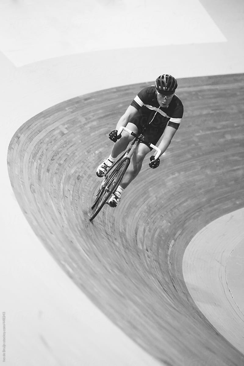 A track cyclist biking fast through the corner of an indoor track in black and white