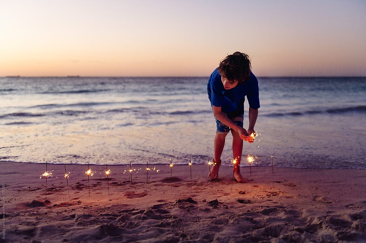 Boy With A Line Of Sparklers In The Sand At The Beach After Sunset By Stocksy Contributor